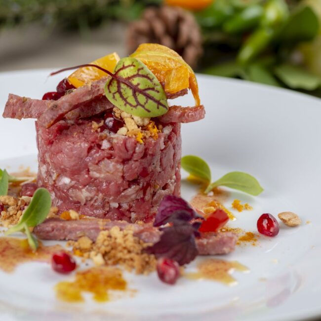 Tartare di girello con guarnizioni di melograno e verdure fresche, servita su un piatto bianco al Ristorante Braceria.